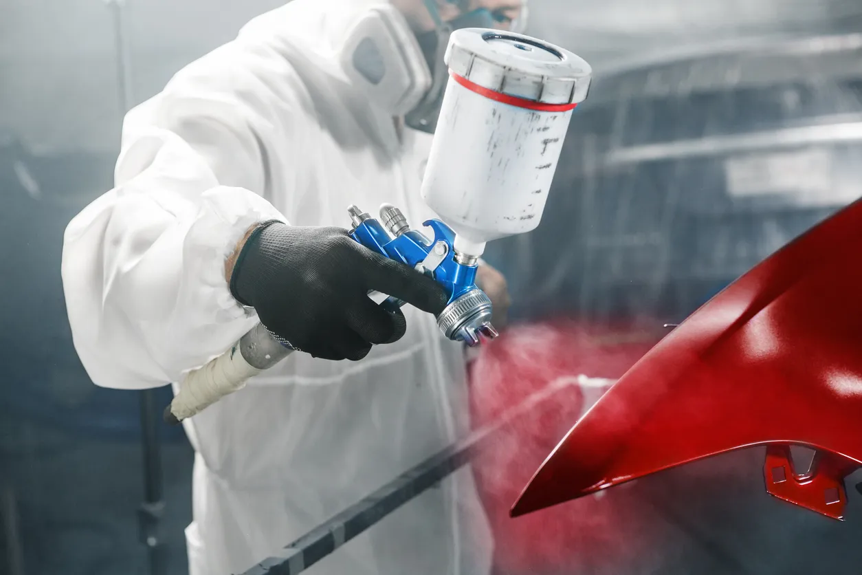 El pintor de automóviles rocía pintura de color rojo a una parte del vehículo con una pistola rociadora en el garaje del tall