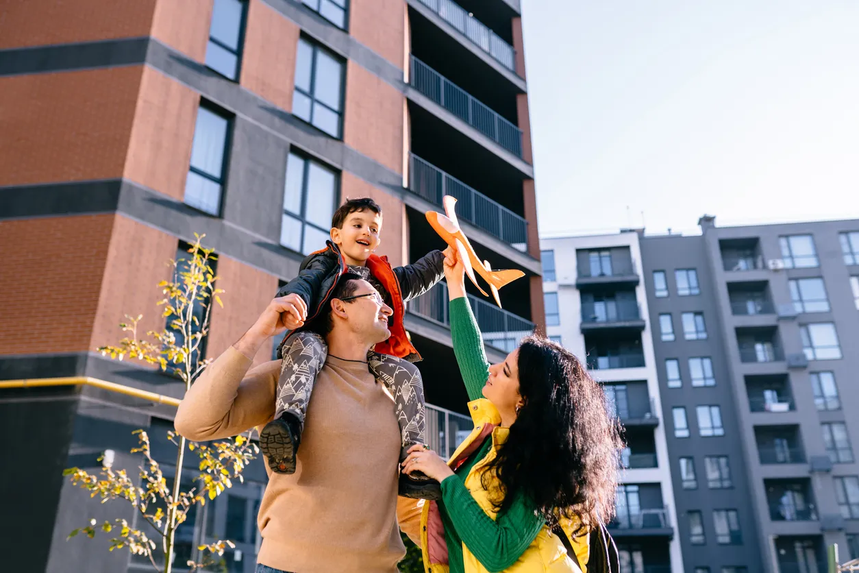 Padre y madre, hijo en el hombro del padre sonriendo con un colorido atuendo informal que sostiene un avión 