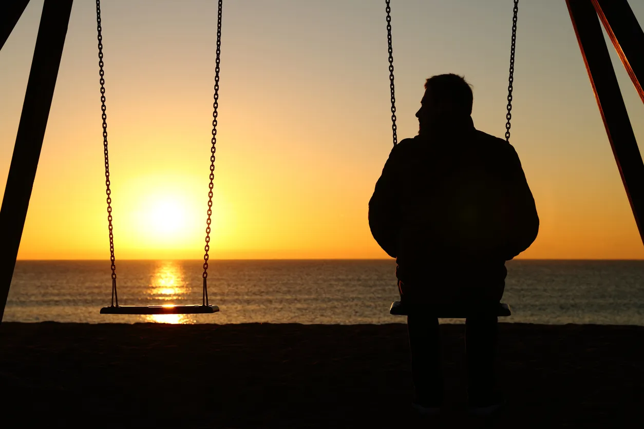 Hombre solo en un columpio mirando el asiento vacío