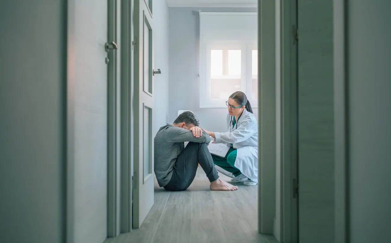 Médico tranquilizador y ayudando al paciente sentado en el piso de la habitación 