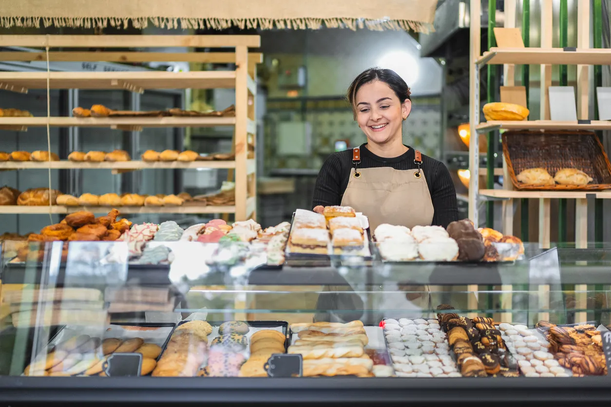 Panadero sonriente arreglando pasteles en vitrina en la panadería