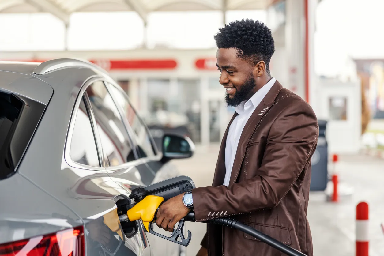 Hombre interracial sonriente llenando el tanque de un coche en una gasolinera.