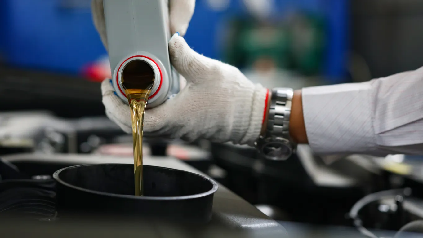 Mecánico de automóviles con guantes vierte aceite de motor en el motor 