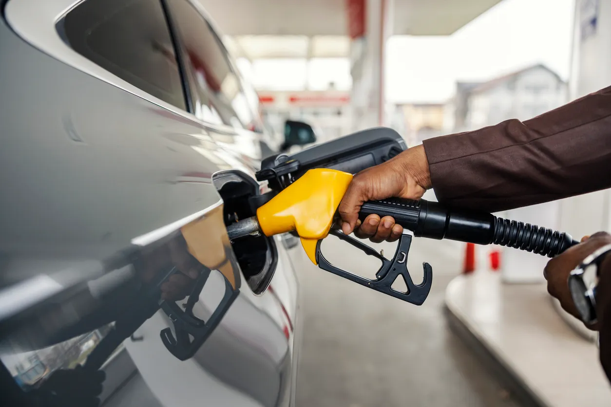 Primer plano de la mano de un hombre interracial sosteniendo la boquilla y vertiendo gasolina en la gasolinera