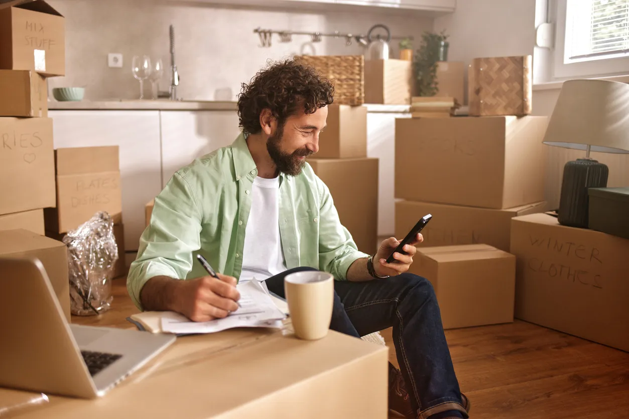 Hombre organizando la mudanza a una nueva casa usando smartphone y lista de comprobación