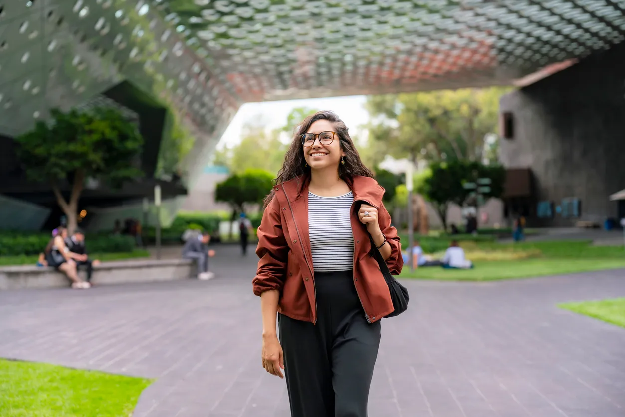 Una joven latina sonriente camina con confianza frente a la Cineteca Nacional en Coyoacán
