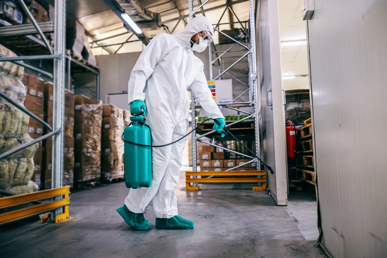 Hombre en traje protector y máscara almacén desinfectante lleno de productos alimenticios