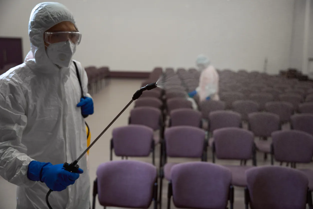 Conserjes profesionales en trajes de inmersión ocupados desinfectando sillas en el edificio 