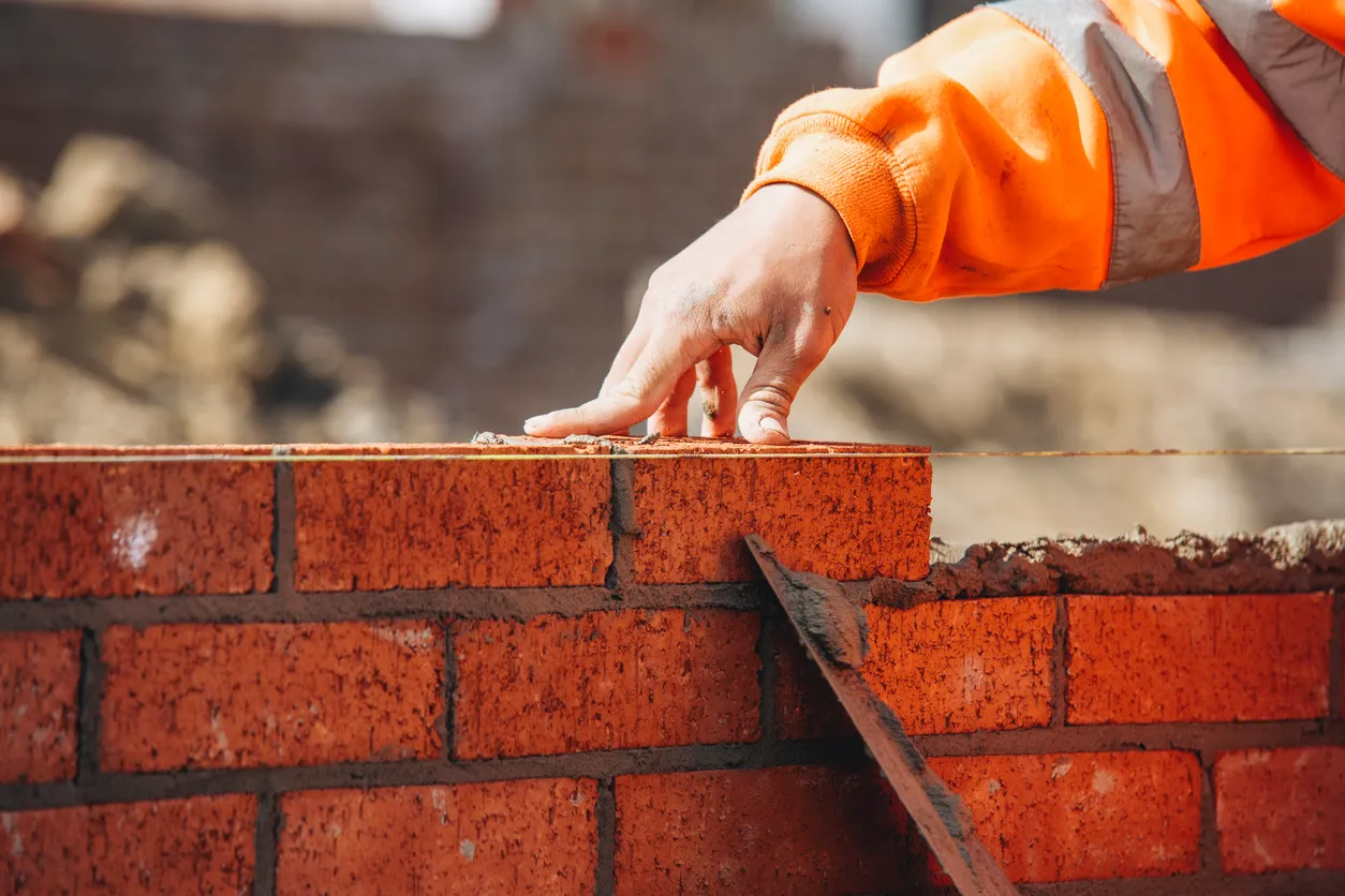 Albañil colocando otro ladrillo en la pared en el sitio de construcción para una pared resistente