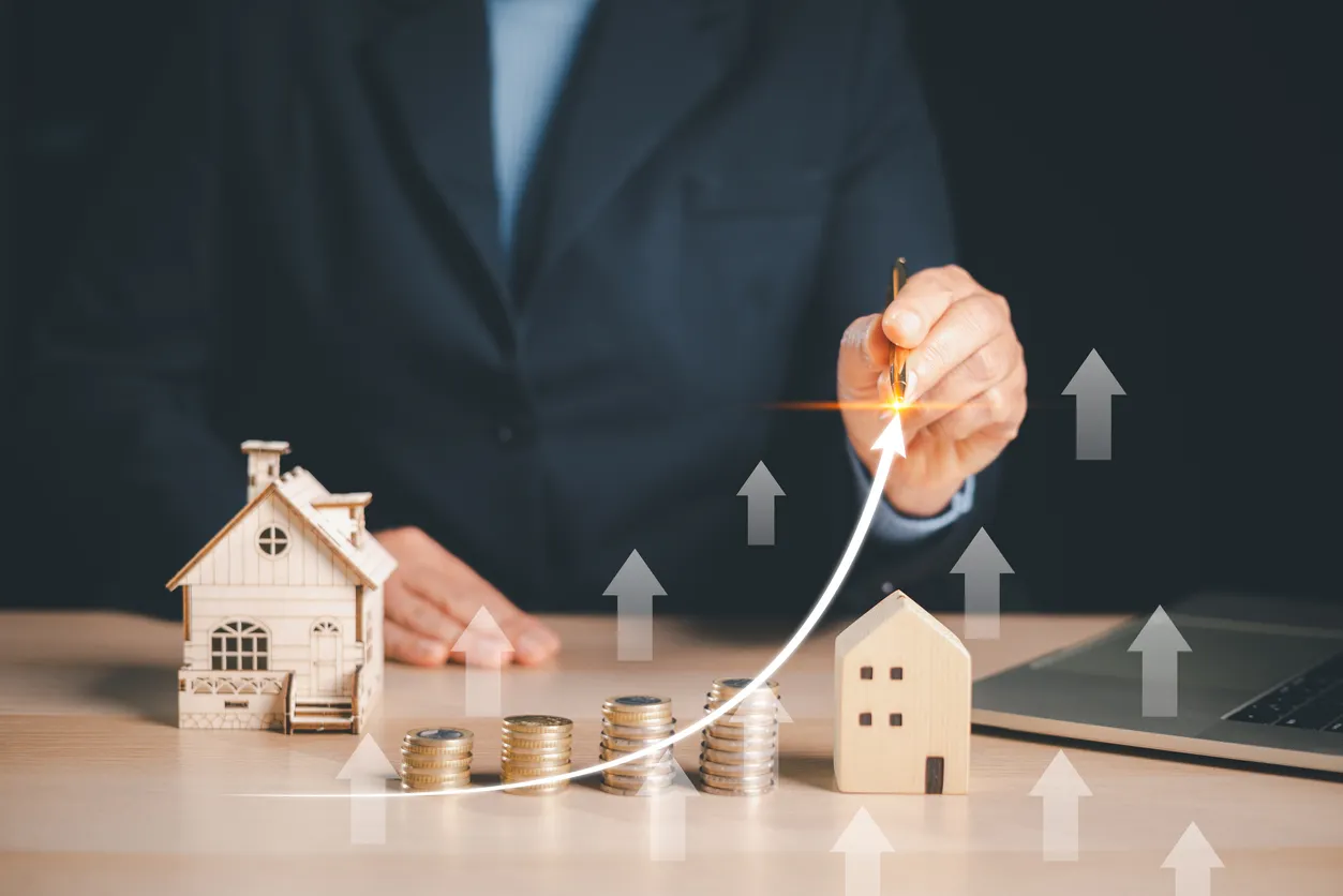 Empresario dibujando flechas ascendentes sobre monedas, modelos de casas, mostrando el crecimiento de la inversión inmobiliar