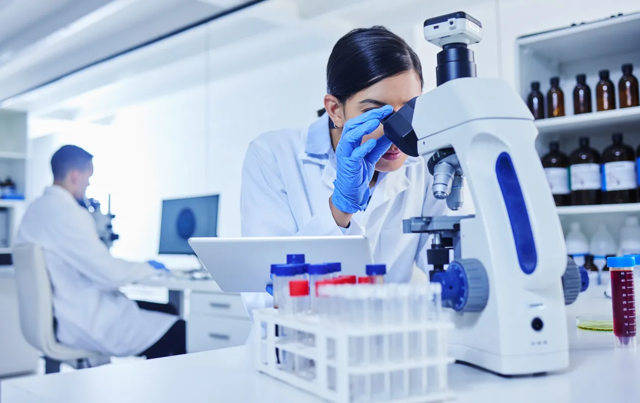 joven científica trabajando con un microscopio y una tableta en su laboratorio