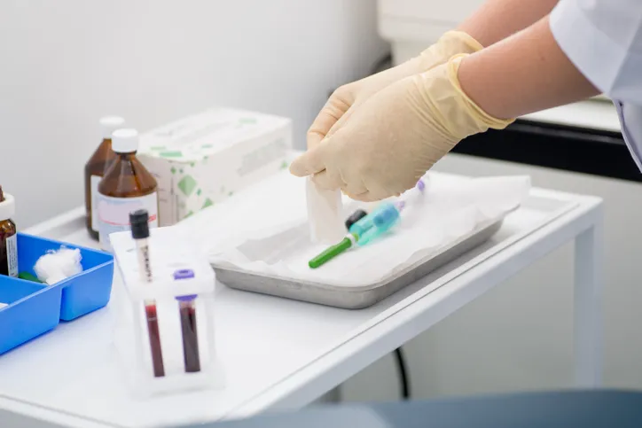 Asistente de laboratorio con guantes preparándose para una extracción de sangre, con tubos para muestras sanguíneas de fondo