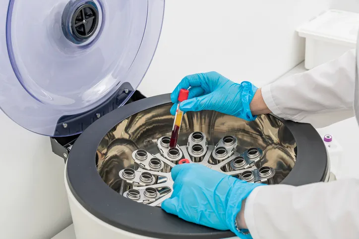 En un laboratorio médico, las manos de una enfermera introducen tubos de ensayo con muestras de sangre en la centrífuga.