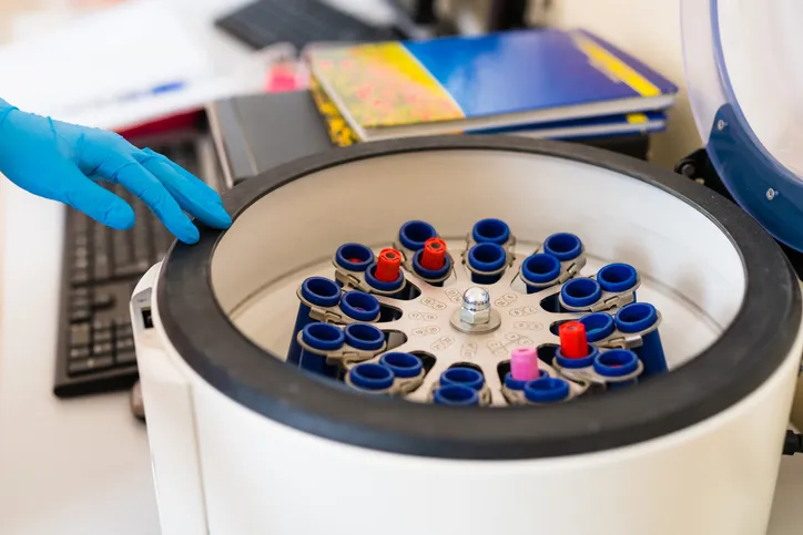 El auxiliar de laboratorio coloca un tubo de ensayo con una muestra para análisis en un aparato centrífugo,