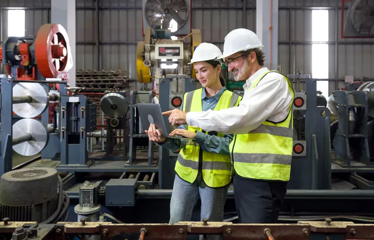 Un gerente de ingeniería sénior capacita a los nuevos empleados en la fábrica de chapa metálica.