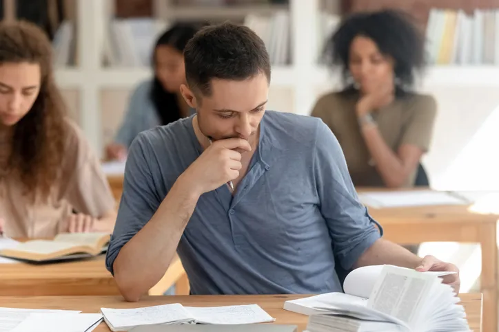 En primer plano un hombre en un escritorio estudiando y detrás varios compañeros