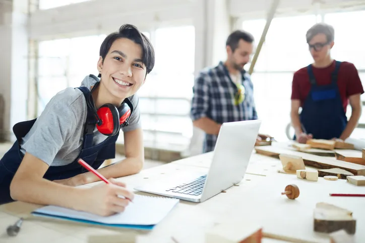 joven trabajadora con overlor y audifonos estudiando y sus compañeros al fondo