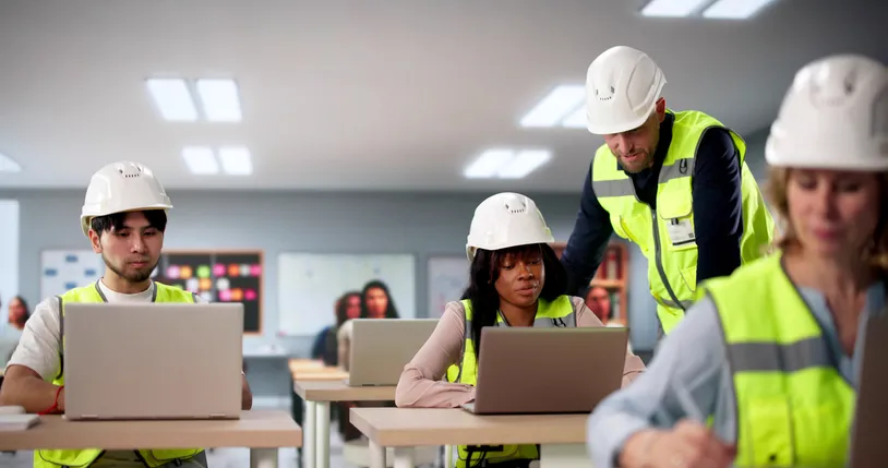 varios trabajadores con uniformes de seguridad y cascos en sala de capacitación