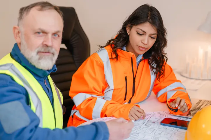 Dos trabajadores con uniforme de trabajo estudiando en área de capacitacióin