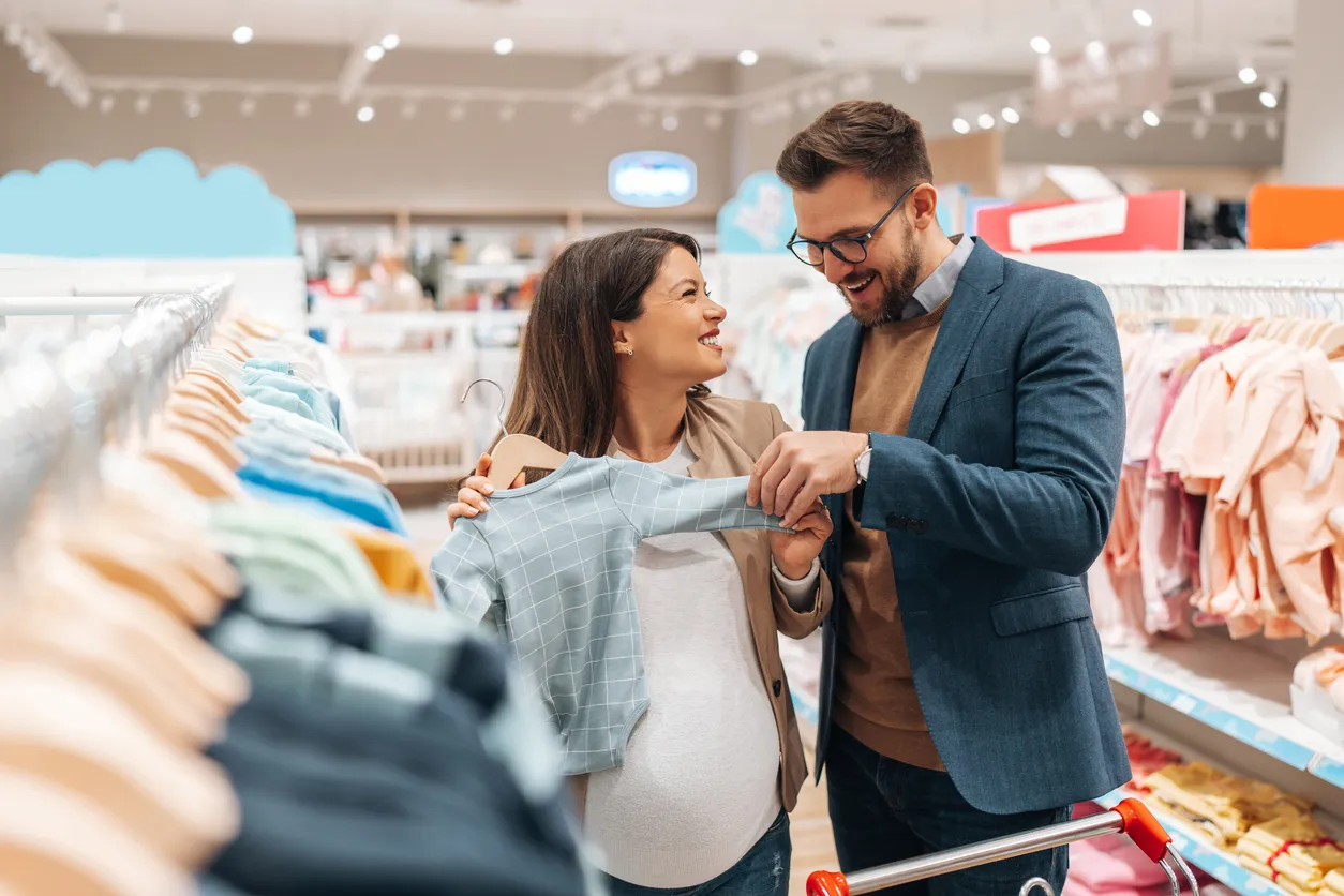 Una atractiva pareja de mediana edad disfruta comprando ropa para su nuevo bebé.