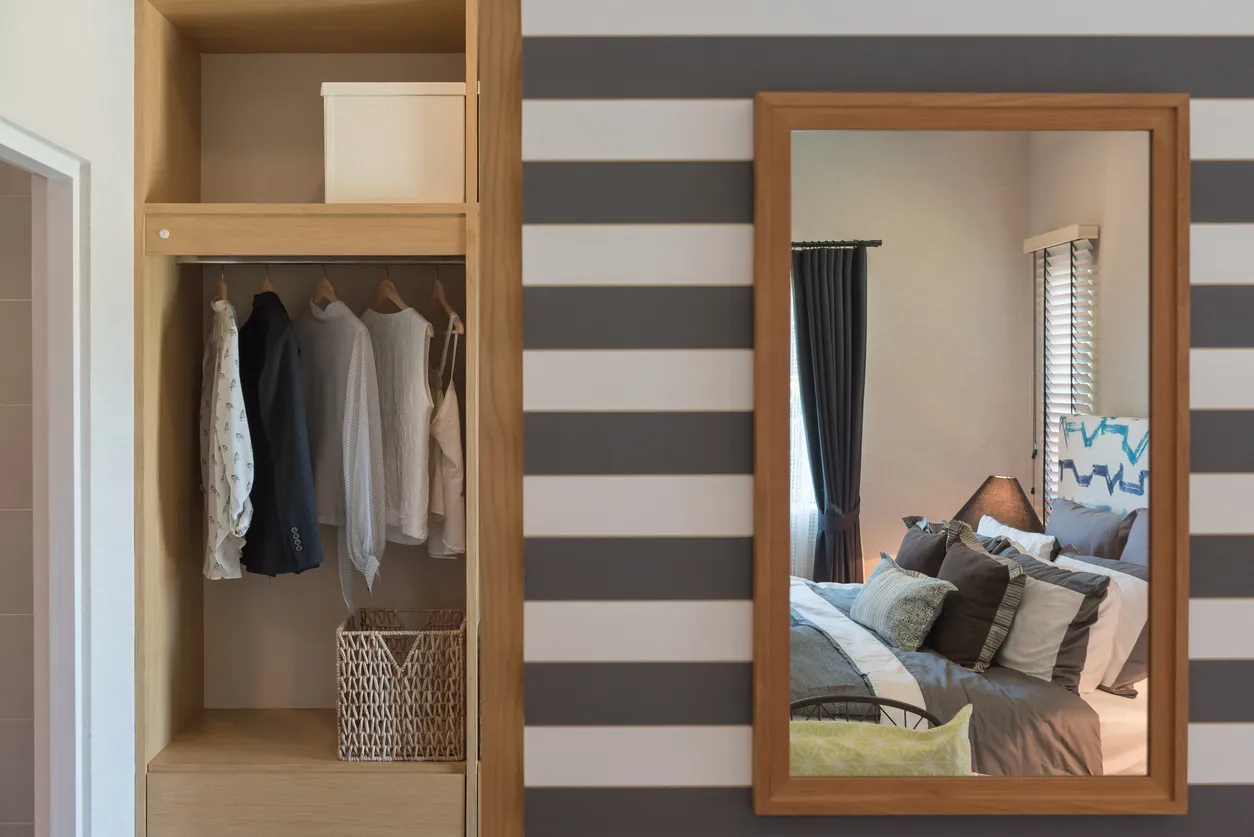 Camisas colgadas en una barra en un moderno armario de madera con el reflejo del dormitorio en gran espejo largo