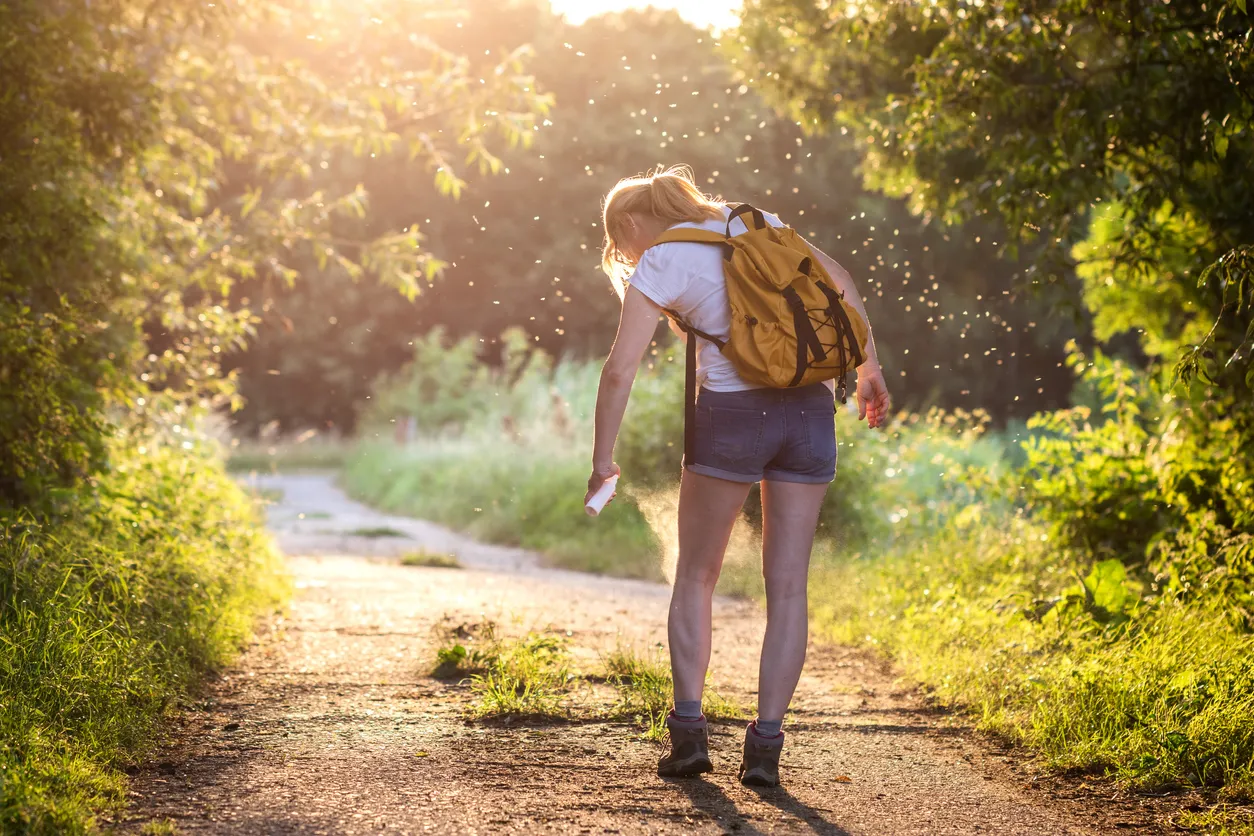 Mujer con mochila aplicando repelente de insectos contra mosquitos y garrapatas al aire libre
