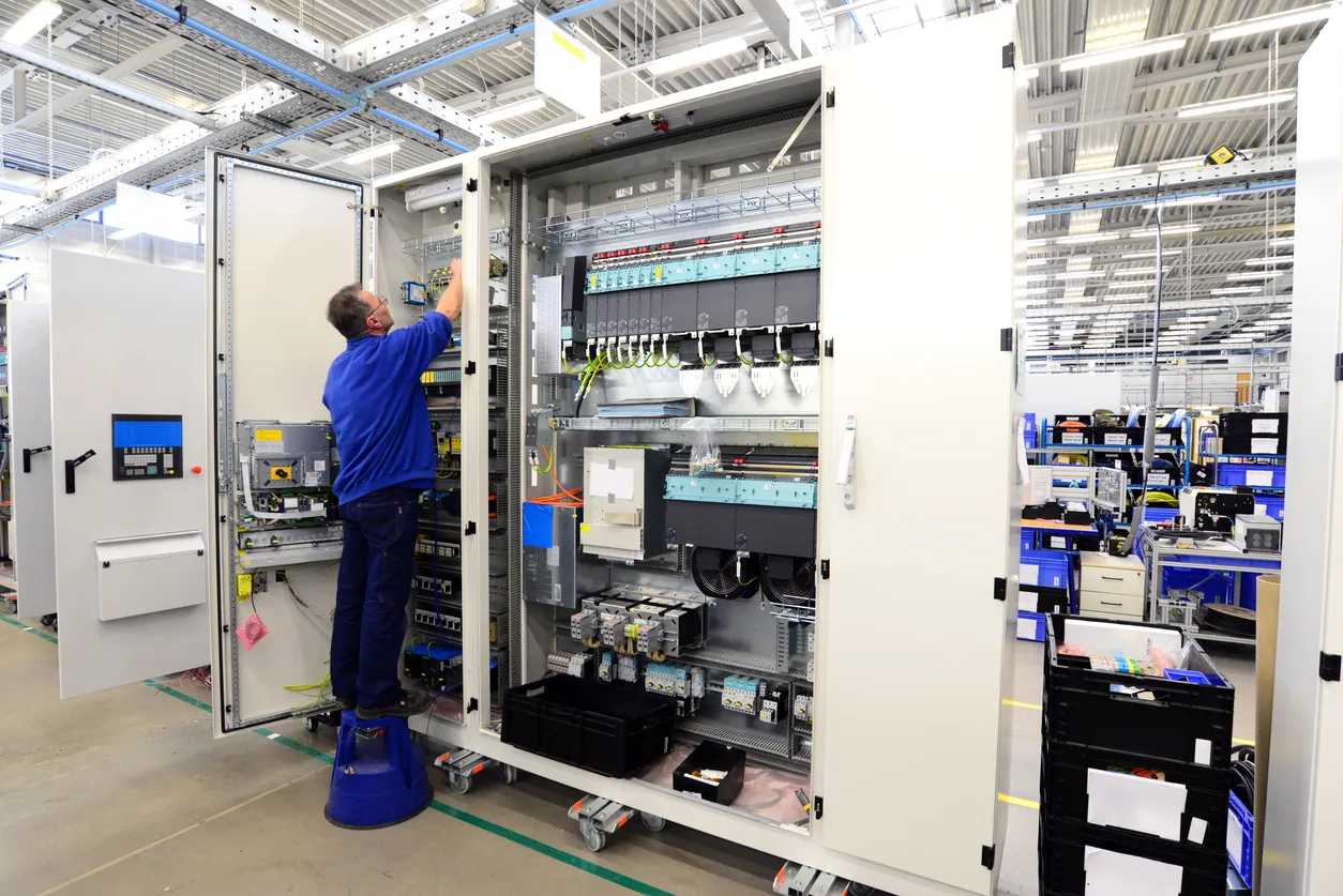 El operador ensambla una máquina en una fábrica: producción de armarios de distribución para plantas industriales