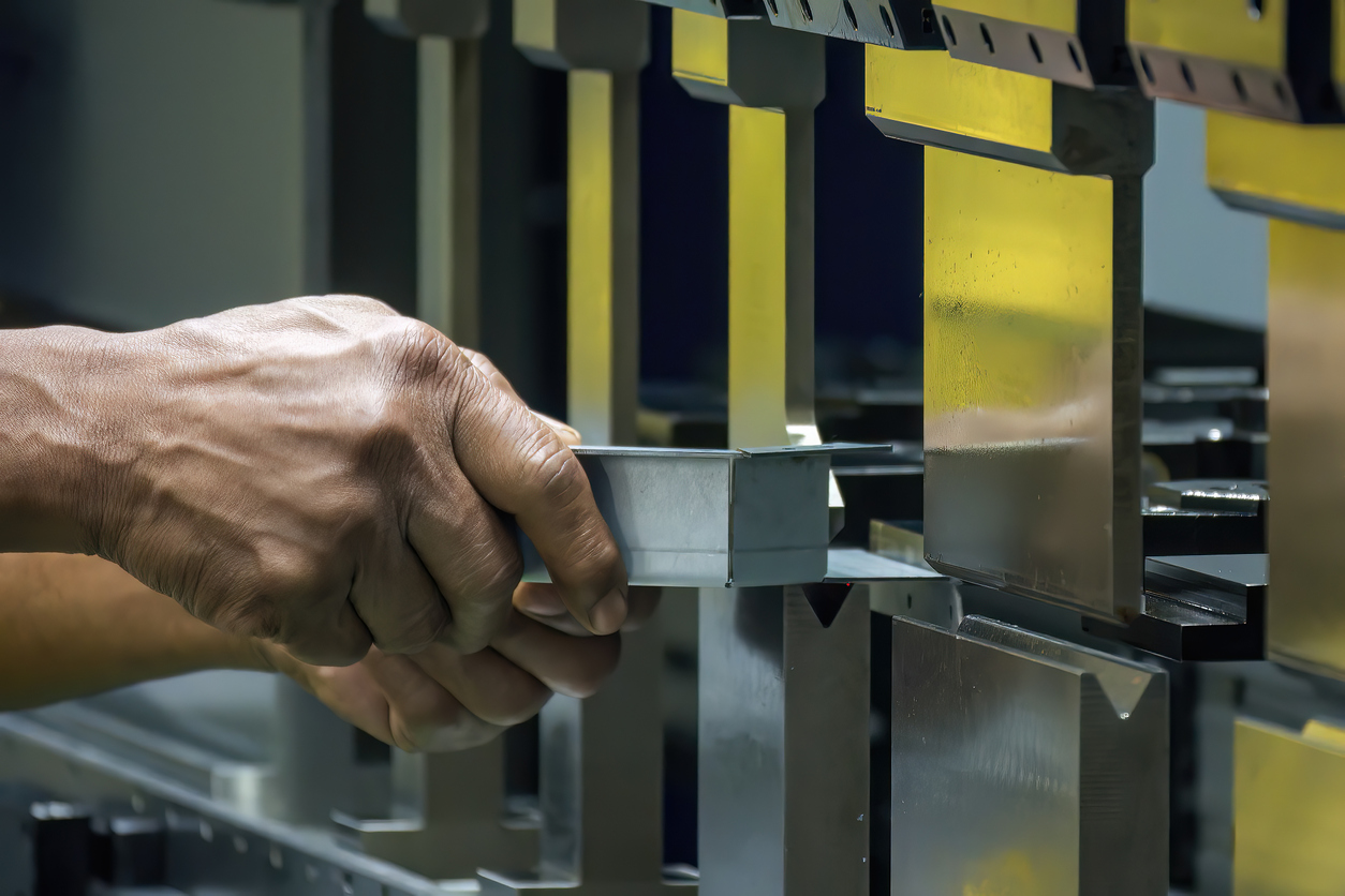 De cerca, el operador de la máquina dobladora sujeta las piezas de chapa