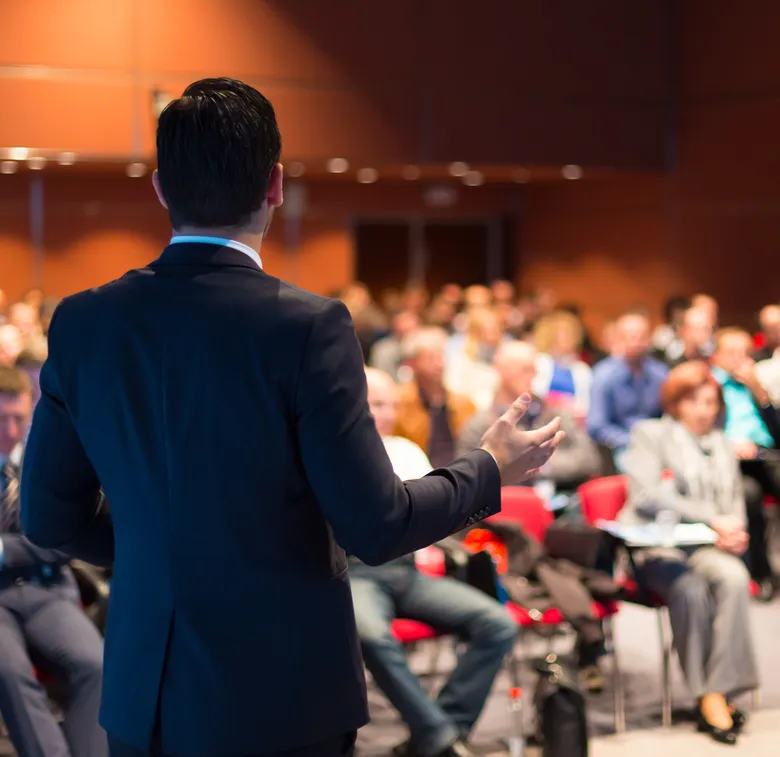 Capacitador hablando frente a un numero grupo de personas al fondo